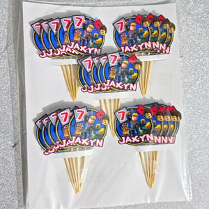 Puede incluir: Adornos para tartas con un dise&ntilde;o azul y amarillo, con el n&uacute;mero 7 y el nombre "JAXYN". Cada adorno tiene un dise&ntilde;o de personaje de dibujos animados y est&aacute; unido a un palillo de madera.