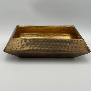 May include: A rectangular, hammered-metal tray with a gold interior and bronze exterior. The tray has a slightly tapered shape and a textured surface. The interior is a bright gold color, while the exterior has a darker, bronze finish.