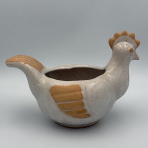 May include: A set of three ceramic mugs with a speckled, matte finish. The mugs are in shades of cream, light gray, and dark gray. Each mug has a simple, minimalist design and a rounded handle.