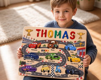 Op de afbeelding: Een rechthoekig houten puzzelbord met een racebaanafbeelding, cartoonauto's en de naam THOMAS in kleurrijke 3D-letters. Het bord toont illustraties van personages zoals McQueen, Mater, Sally, Doc Hudson, Chick Hicks, Cruz Ramirez, Ramone, Luigi, Guido en Jackson Storm.