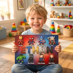 May include: A rectangular wooden plaque featuring the name ETHAN in large, colorful, stylized letters. Surrounding the name are eight small, cartoon-style superhero figures: Iron Man, Spider-Man, Captain America, Thor, Hulk, Black Panther, Doctor Strange, and Black Widow, each labeled with their respective names.