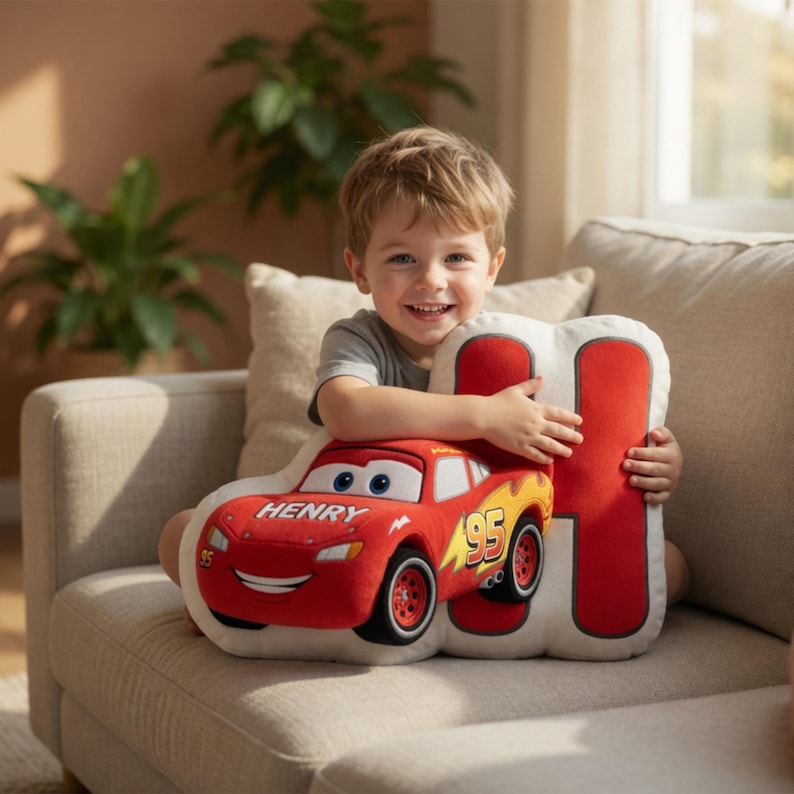 May include: A plush pillow shaped like the character Lightning McQueen from the movie Cars. The red car has the number 95 and the name "HENRY" printed on it. The pillow is being held by a child.