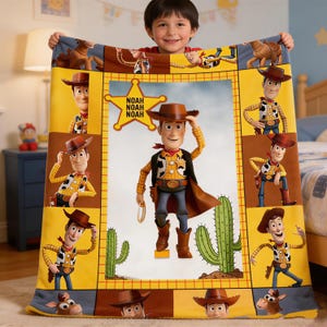 Op de afbeelding: Een kleurrijke deken met het personage Woody uit de film Toy Story. De deken heeft een gele rand met afbeeldingen van Woody en een centraal beeld van Woody met een cactus en een ster met de naam "NOAH".
