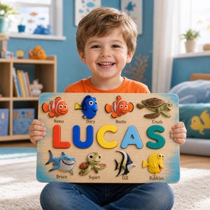 Peut inclure: Un puzzle en bois rectangulaire affichant le prénom LUCAS en grandes lettres colorées. La planche comprend des figurines en relief représentant diverses créatures marines étiquetées avec leurs noms : Nemo, Dory, Marlin, Crush, Bruce, Squirt, Gill et Bubbles.