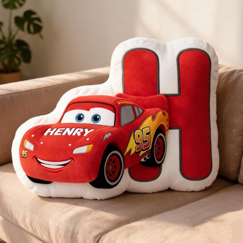 May include: A plush pillow in the shape of Lightning McQueen from the Cars movie, with the name "HENRY" on the front. The pillow is red with a white background and a large red letter "H".
