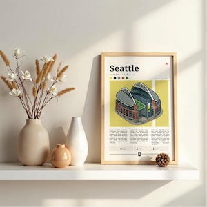 Peut inclure: Une affiche encadrée représentant le stade Lumen Field de Seattle, avec le mot "Seattle" en haut. L'affiche est dans un cadre en bois clair et repose sur une étagère blanche avec des vases et des fleurs décoratives.