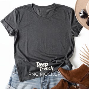 May include: A dark gray t-shirt with rolled-up sleeves, knotted at the waist, and the text "Deep Trench PNG MOCKUP" in white. The shirt is paired with denim shorts, brown boots, a hat, and sunglasses.