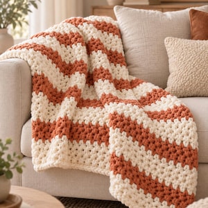 Peut inclure: Un plaid en tricot épais présentant un motif à chevrons répétitif avec des rayures alternées de fil crème et orange brûlé. Le fil épais et texturé crée une surface douce et en relief avec un motif en zigzag constant sur tout le tissu.