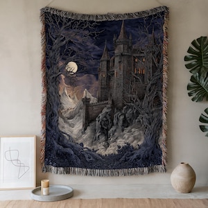 May include: Woven tapestry featuring a gothic castle scene under a moonlit sky. The artwork depicts a dark, foreboding castle with tall spires, surrounded by bare trees and swirling clouds. The tapestry has a fringed edge and is primarily dark blue, gray, and white.