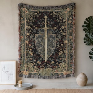 May include: A tapestry featuring a sword and shield design, set against a dark floral background. The tapestry has a fringed edge and is hung on a neutral wall. The color palette includes shades of black, green, beige, and red.