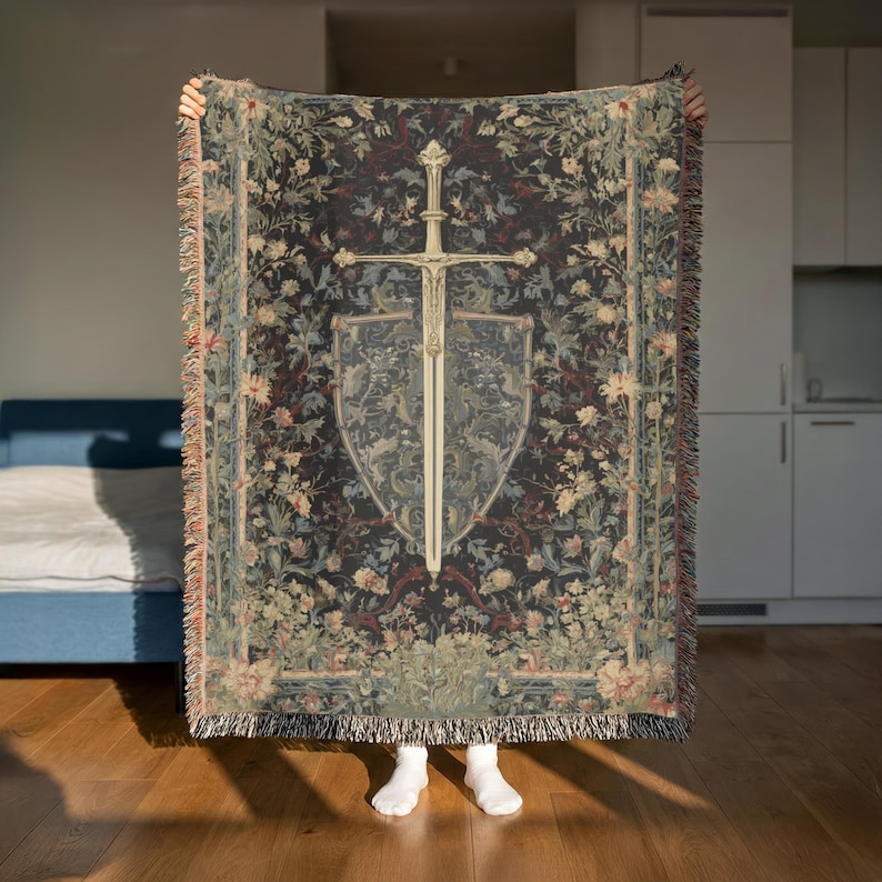 May include: A tapestry-style throw blanket with a dark background and floral patterns. The center features a sword and shield design in cream and gray. The blanket has fringed edges.
