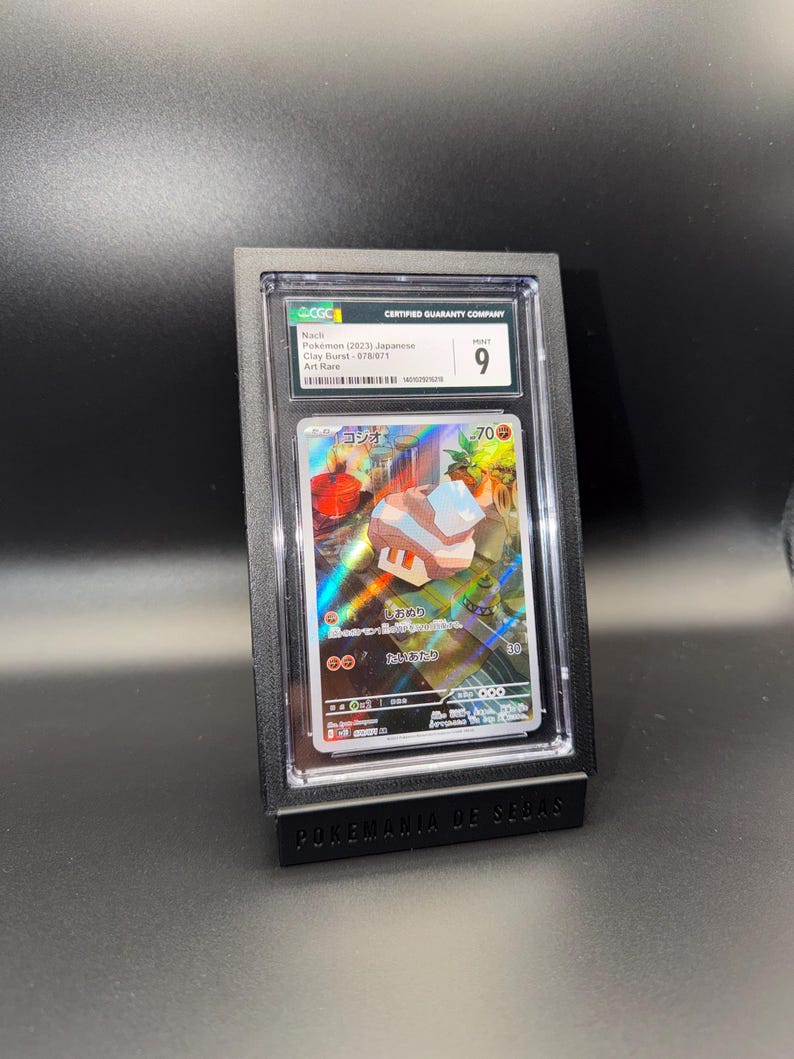 May include: A graded Pok&eacute;mon card in a black display case. The card features Japanese text and a colorful illustration. The case is labeled "CERTIFIED GUARANTY COMPANY" and has a grade of 9. The base of the display reads "POKEMANIA DE SEBAS."