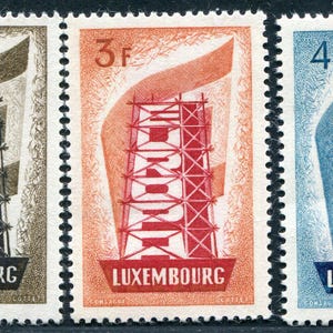 Op de afbeelding: Drie vintage postzegels uit Luxemburg. Elke postzegel toont een gestileerd torenontwerp met een lintachtig element. De postzegels zijn in tinten bruin, oranje en blauw, met de waardeaanduiding en "LUXEMBOURG" erop gedrukt.