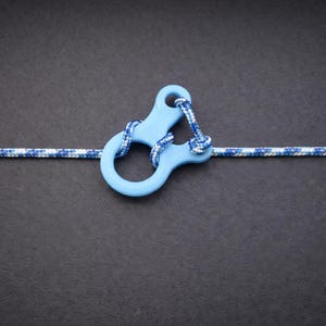 Pode incluir: Um conector azul claro tipo mosquetão com uma corda azul e branca que o atravessa. O conector é feito de um material liso e tem uma forma única. A corda é de tamanho padrão e é usada para várias atividades ao ar livre.