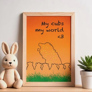 May include: A framed art print with an orange and yellow gradient background. The print features a black outline of a lion and cubs, with the text "My cubs my world <3". A stuffed bunny and potted plant are on the shelf.