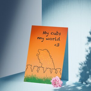 May include: An orange card with the text "My cubs my world <3" and a black illustration of a lion and cubs. A pink flower rests at the bottom right corner. The card is set against a blue and white background.