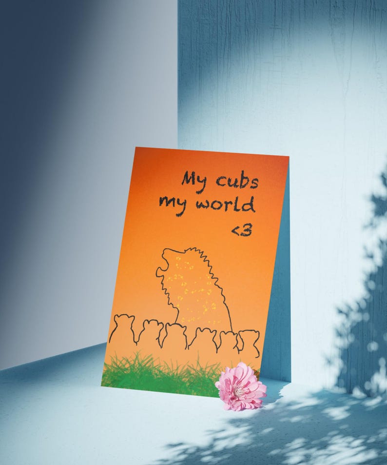 May include: An orange card with the text "My cubs my world <3" and a black illustration of a lion and cubs. A pink flower rests at the bottom right corner. The card is set against a blue and white background.