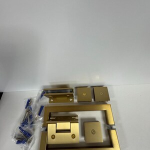 May include: A collection of new, gold-colored shower door hardware components. The set includes hinges, brackets, and a handle, along with screws and wall anchors. The hardware is designed for a modern bathroom aesthetic.