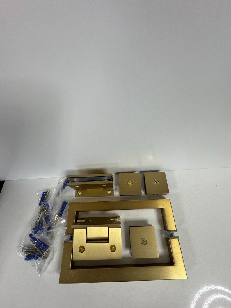 May include: A collection of new, gold-colored shower door hardware components. The set includes hinges, brackets, and a handle, along with screws and wall anchors. The hardware is designed for a modern bathroom aesthetic.