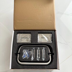 May include: A stainless steel shower door hardware kit, presented in an open cardboard box. The kit includes hinges, a handle, and mounting hardware, all neatly arranged in a black foam insert. The components are sealed in clear plastic.