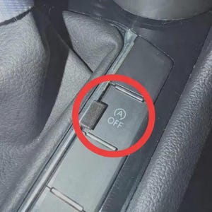 May include: Close-up of a black car interior. The image focuses on a black button with the text "A OFF" and a circular symbol. The button is part of a console with other controls.
