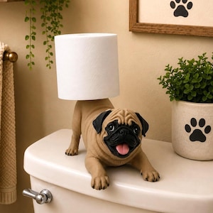 May include: A tan and black pug-shaped toilet paper holder featuring a realistic dog figure with a black muzzle, floppy ears, and an open mouth with a pink tongue, designed to support a single roll of white toilet paper on its back.