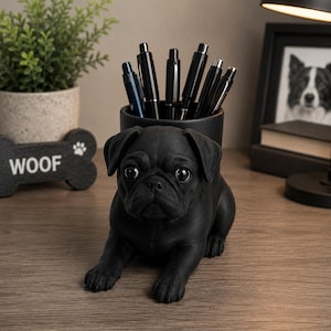 May include: A matte black desk organizer shaped like a pug dog, featuring a cylindrical container on its back filled with several black pens. The pug is depicted in a lying position with detailed facial features, including large eyes and ears.