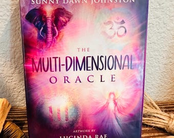May include: The Multi-Dimensional Oracle deck by Sunny Dawn Johnston, with artwork by Lucinda Rae. The cover features an elephant, the Om symbol, an angel, and the number 111, all set against a vibrant, colorful background.
