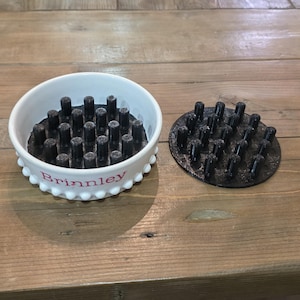 May include: A white ceramic soap dish with a scalloped edge and the name "Brinnley" in pink lettering. The dish contains black cylindrical soap holders. A separate black soap holder is next to the dish.