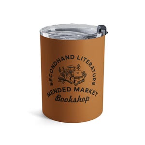 May include: A matte brown tumbler with a clear plastic lid and a black sliding closure. The front features a black graphic of stacked books and a teacup, surrounded by the text "SECONDHAND LITERATURE MENDED MARKET Bookshop" in black.