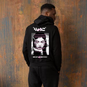 Puede incluir: Sudadera con capucha negra con un gráfico en la espalda. El gráfico presenta un retrato de una mujer con texto japonés encima y debajo de la imagen. El retrato es en tonos rosa y blanco.