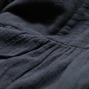 May include: Close-up shot of dark grey fabric, showing texture and pleating. The material looks soft and slightly creased, possibly linen or cotton. The image highlights the details of the textile.