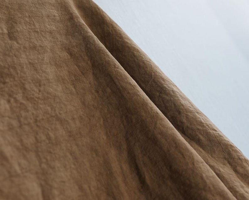 May include: Close-up of a brown fabric with a textured surface. The fabric is folded, creating shadows and highlights that emphasize its texture. The background is a light, neutral color.