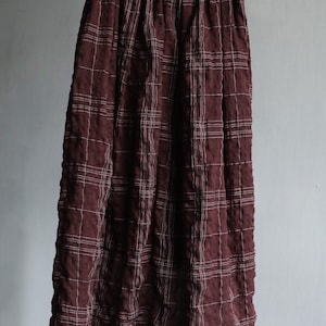 May include: A long, burgundy skirt with a white grid pattern, hanging from a hanger. The skirt has an elastic waistband and a flowing silhouette, suitable for casual wear.