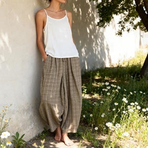 May include: A white spaghetti strap vest top paired with loose-fitting, wide-leg trousers featuring a brown and tan plaid pattern. The trousers have a drawstring waist and a relaxed, flowing silhouette that extends to the lower calf area.
