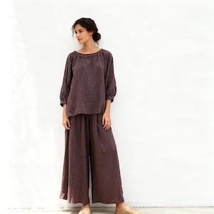 May include: A two-piece outfit in a muted purple hue. The set comprises a long-sleeved top with a round neckline and wide-leg trousers. The ensemble is crafted from a soft, flowing material, suitable for relaxed occasions.