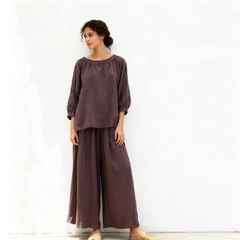 May include: A two-piece outfit in a muted purple hue. The set comprises a long-sleeved top with a round neckline and wide-leg trousers. The ensemble is crafted from a soft, flowing material, suitable for relaxed occasions.