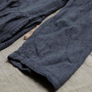 May include: Close-up of a dark blue long-sleeved garment. The fabric has a textured, slightly wrinkled appearance, with visible seams and stitching. The sleeve cuff is visible, suggesting a casual, comfortable design.