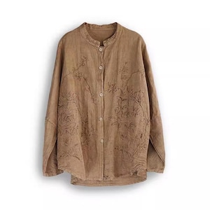 May include: A long-sleeved, button-down shirt in a light brown hue. The shirt features a mandarin collar and is adorned with embroidered floral patterns across the front. The fabric appears to be lightweight, suitable for warmer weather.