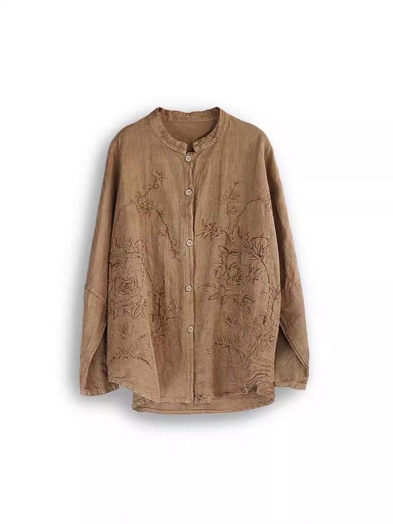 May include: A long-sleeved, button-down shirt in a light brown hue. The shirt features a mandarin collar and is adorned with embroidered floral patterns across the front. The fabric appears to be lightweight, suitable for warmer weather.