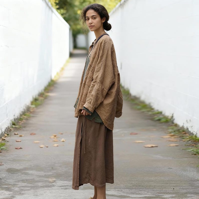 May include: A woman wearing a layered outfit of brown and green clothing. The outfit includes a loose-fitting, long-sleeved brown jacket, a green top, and a long brown skirt. The outfit is made of a soft, natural fabric.
