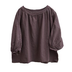May include: A dark mauve blouse with a round neckline and three-quarter sleeves. The sleeves have a gathered, puffy design at the elbow. The top is made of a soft, textured fabric, and the overall style is casual and comfortable.