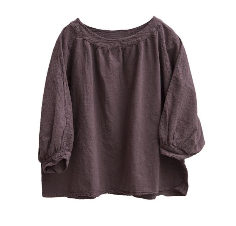 May include: A dark mauve blouse with a round neckline and three-quarter sleeves. The sleeves have a gathered, puffy design at the elbow. The top is made of a soft, textured fabric, and the overall style is casual and comfortable.