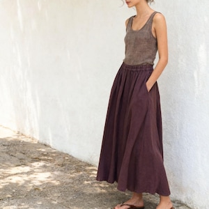 May include: A dark brown sleeveless tank top with a scoop neckline paired with a long, flowing dark plum skirt. The skirt features a gathered elastic waistband and deep side pockets, falling to the ankles in a simple, unadorned silhouette.