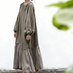 Puede incluir: Vestido largo verde oliva con mangas largas y falda escalonada. El vestido tiene una silueta suelta y fluida y est&aacute; hecho de una tela suave y natural. La modelo lleva sandalias tejidas. El vestido es adecuado para ropa casual.