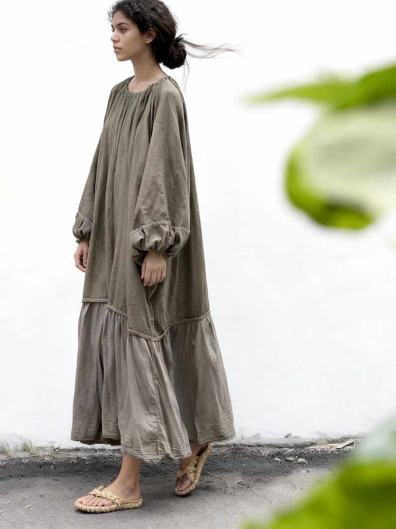 Puede incluir: Vestido largo verde oliva con mangas largas y falda escalonada. El vestido tiene una silueta suelta y fluida y est&aacute; hecho de una tela suave y natural. La modelo lleva sandalias tejidas. El vestido es adecuado para ropa casual.