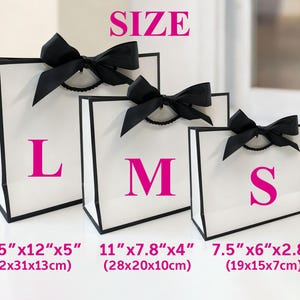 May include: Three white gift bags with black trim and black bows. The bags are labelled with the letters L, M, and S in pink. Measurements are provided in inches and centimetres: 16.5"x12"x5" (42x31x13cm), 11"x7.8"x4" (28x20x10cm), and 7.5"x6"x2.8" (19x15x7cm). The word "SIZE" is at the top.