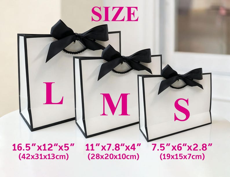 May include: Three white gift bags with black trim and black bows. The bags are labelled with the letters L, M, and S in pink. Measurements are provided in inches and centimetres: 16.5"x12"x5" (42x31x13cm), 11"x7.8"x4" (28x20x10cm), and 7.5"x6"x2.8" (19x15x7cm). The word "SIZE" is at the top.