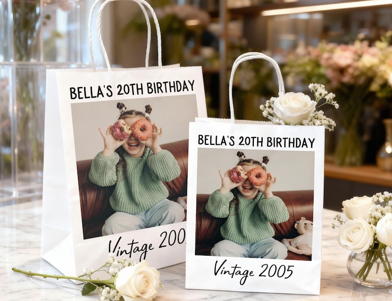 Pu&ograve; includere: Due sacchetti regalo di carta bianca con manici bianchi. Ogni sacchetto presenta una foto di una giovane persona che tiene delle ciambelle sugli occhi. Il testo sui sacchetti recita "BELLA'S 20TH BIRTHDAY" e "Vintage 2005" e "Vintage 200".
