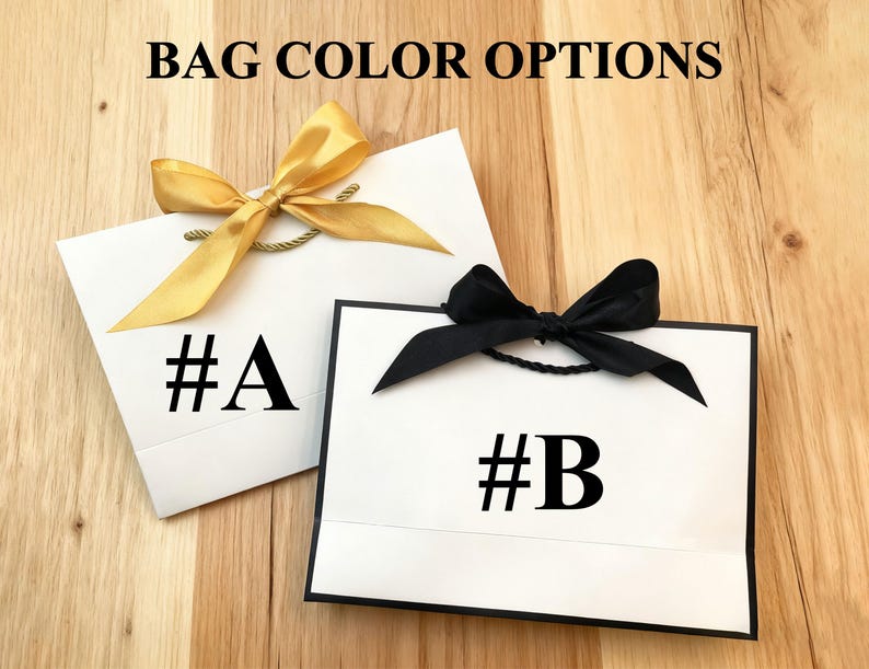 May include: Two white gift bags with black text and bows. One bag has a gold bow and the text "#A". The other bag has a black bow and the text "#B". The words "BAG COLOR OPTIONS" are at the top.